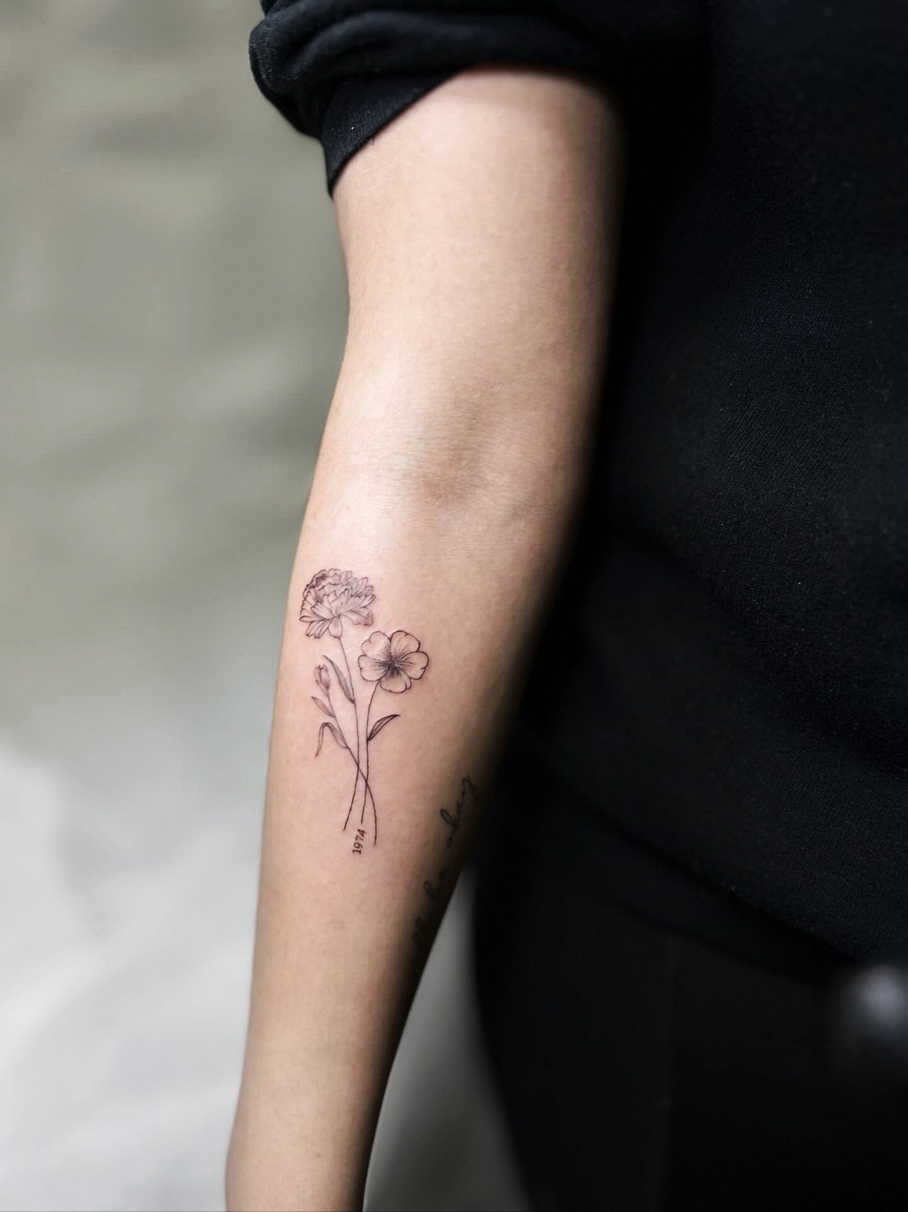 Fine line carnation and poppy forearm tattoo with a tiny 1974 by On Point Fine Line Tattoo Studio, Woodridge IL