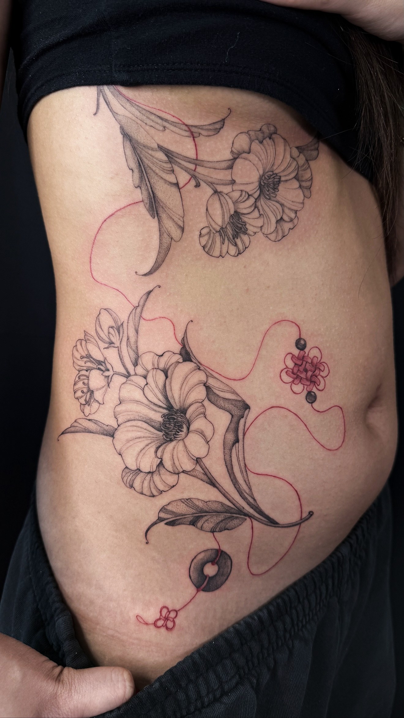 Fine line floral side tattoo with red thread and knot charms by On Point Fine Line Tattoo Studio, Woodridge IL